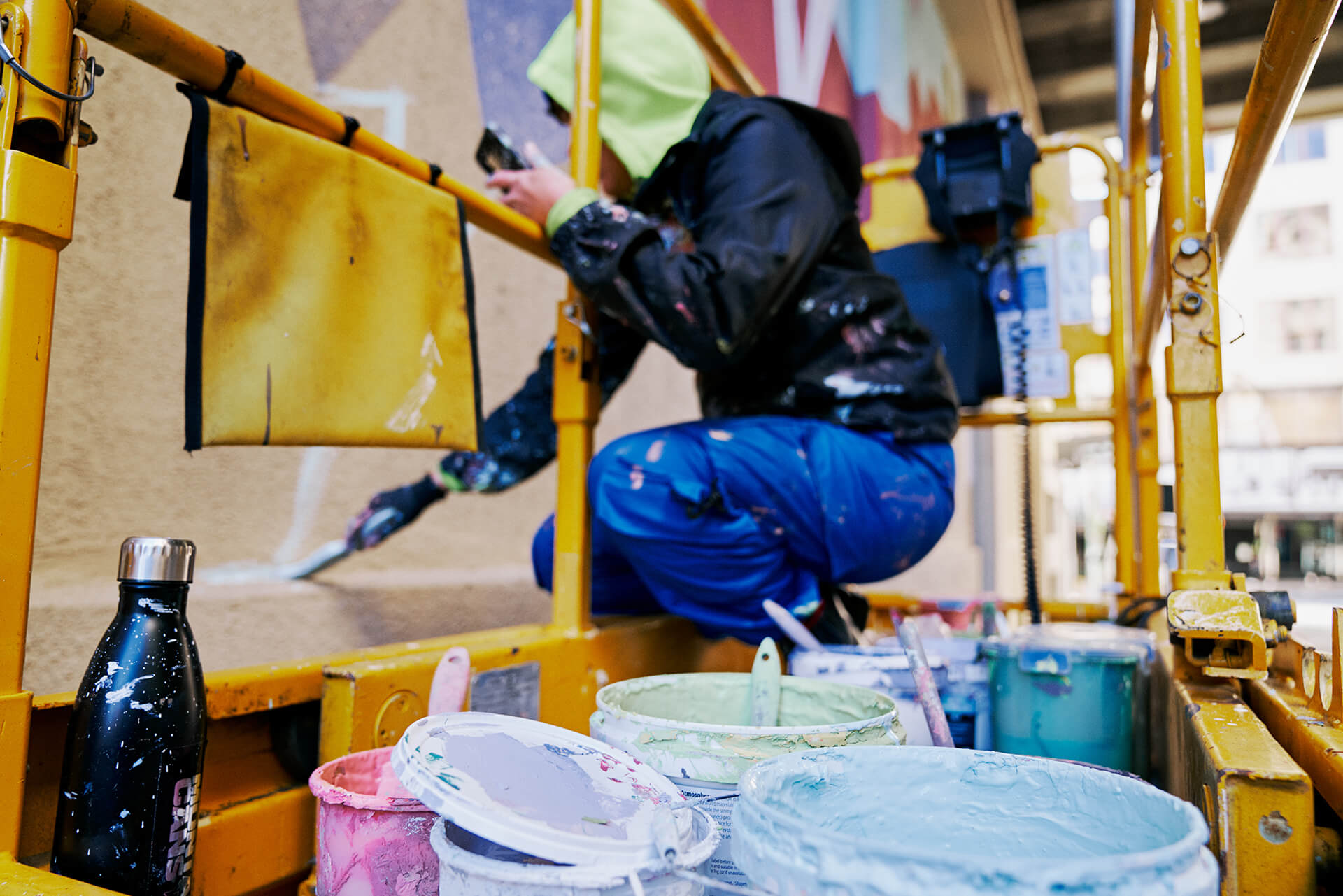 Artist on a scissors lift painting a geometric multicoloured wall mural produced by VANDAL for Mirvac