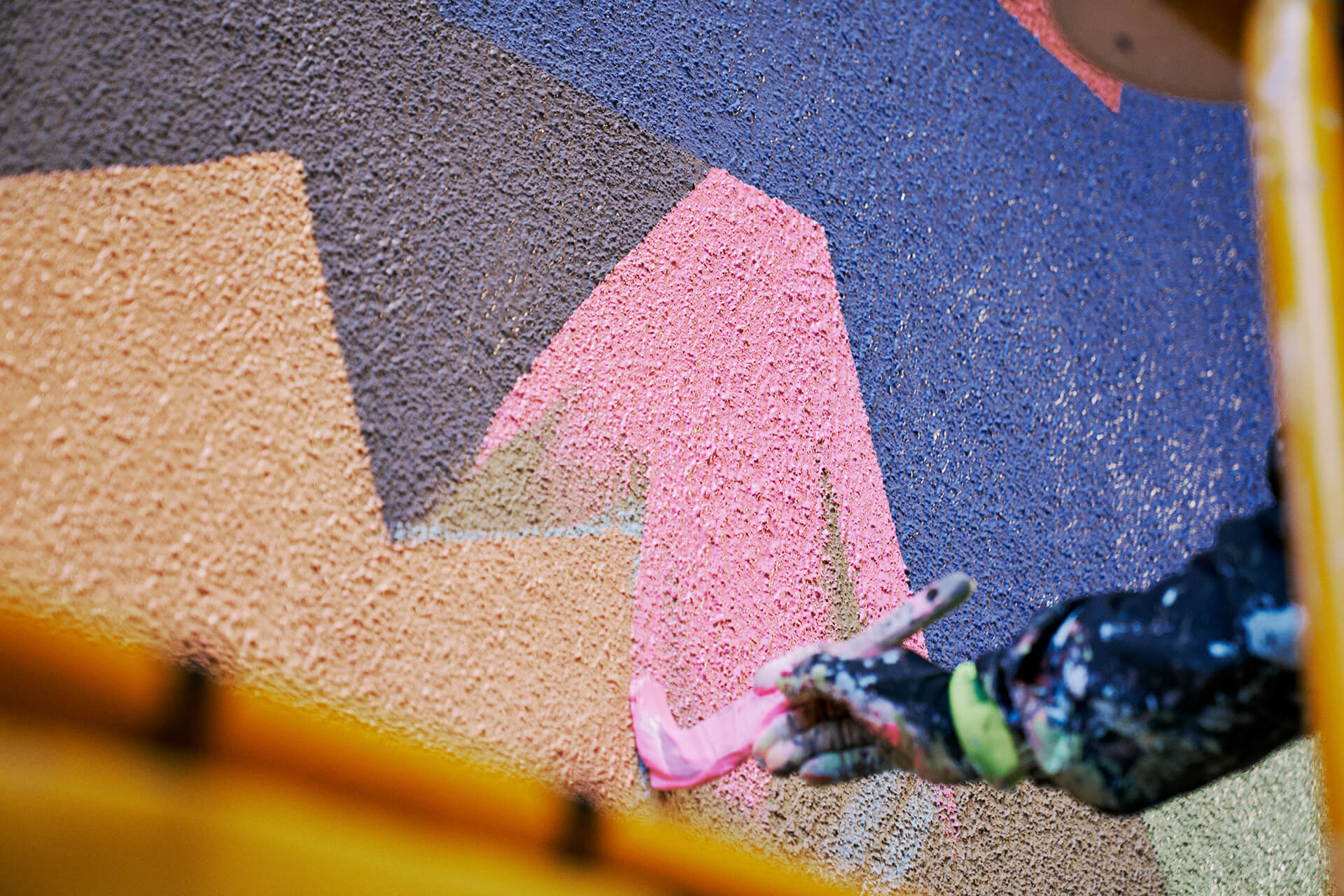 Close up of a hand applying paint to a wall to create a geometric multicoloured wall mural produced by VANDAL for Mirvac