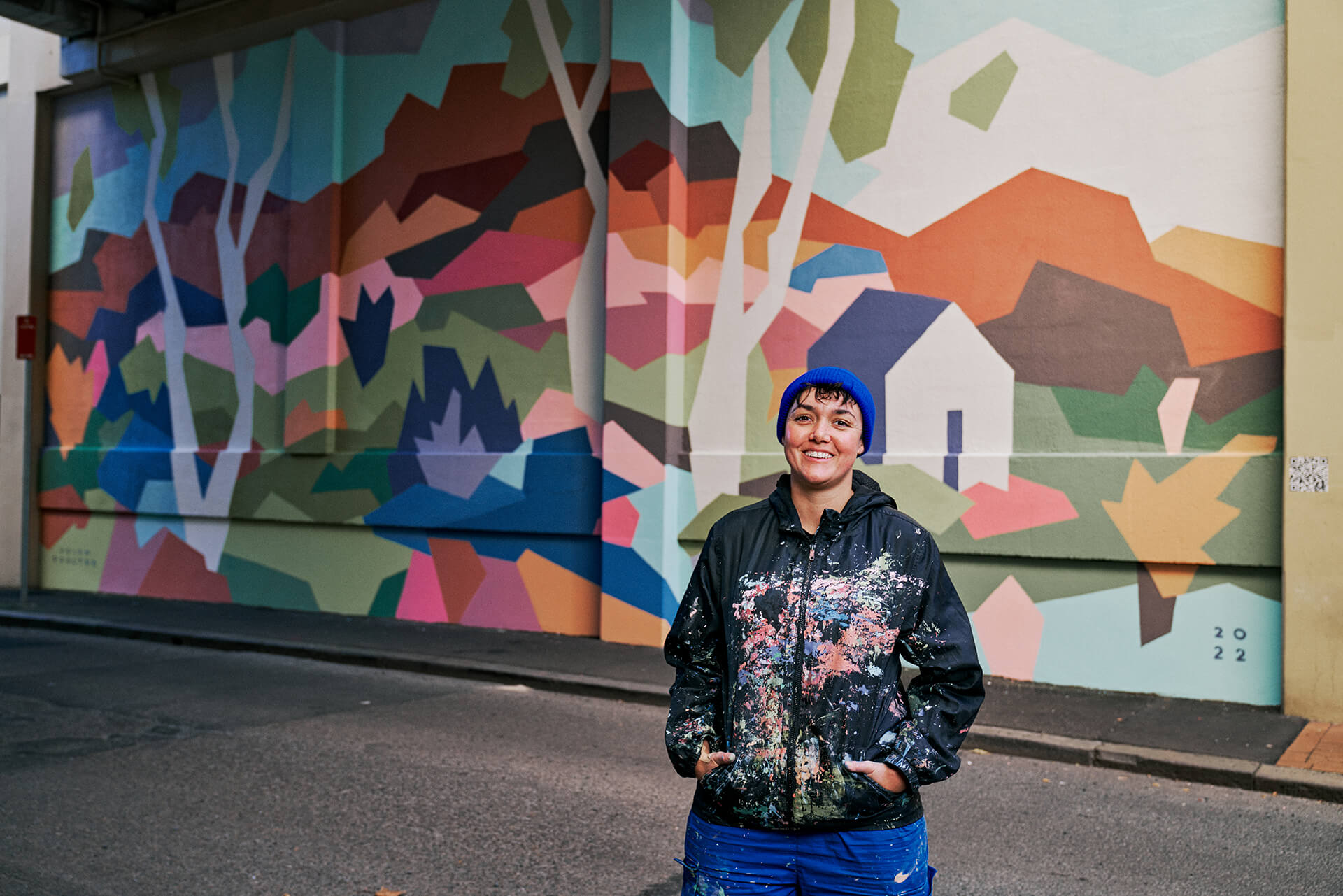Artist standing proudly in front of geometric multicoloured wall mural produced by VANDAL for Mirvac