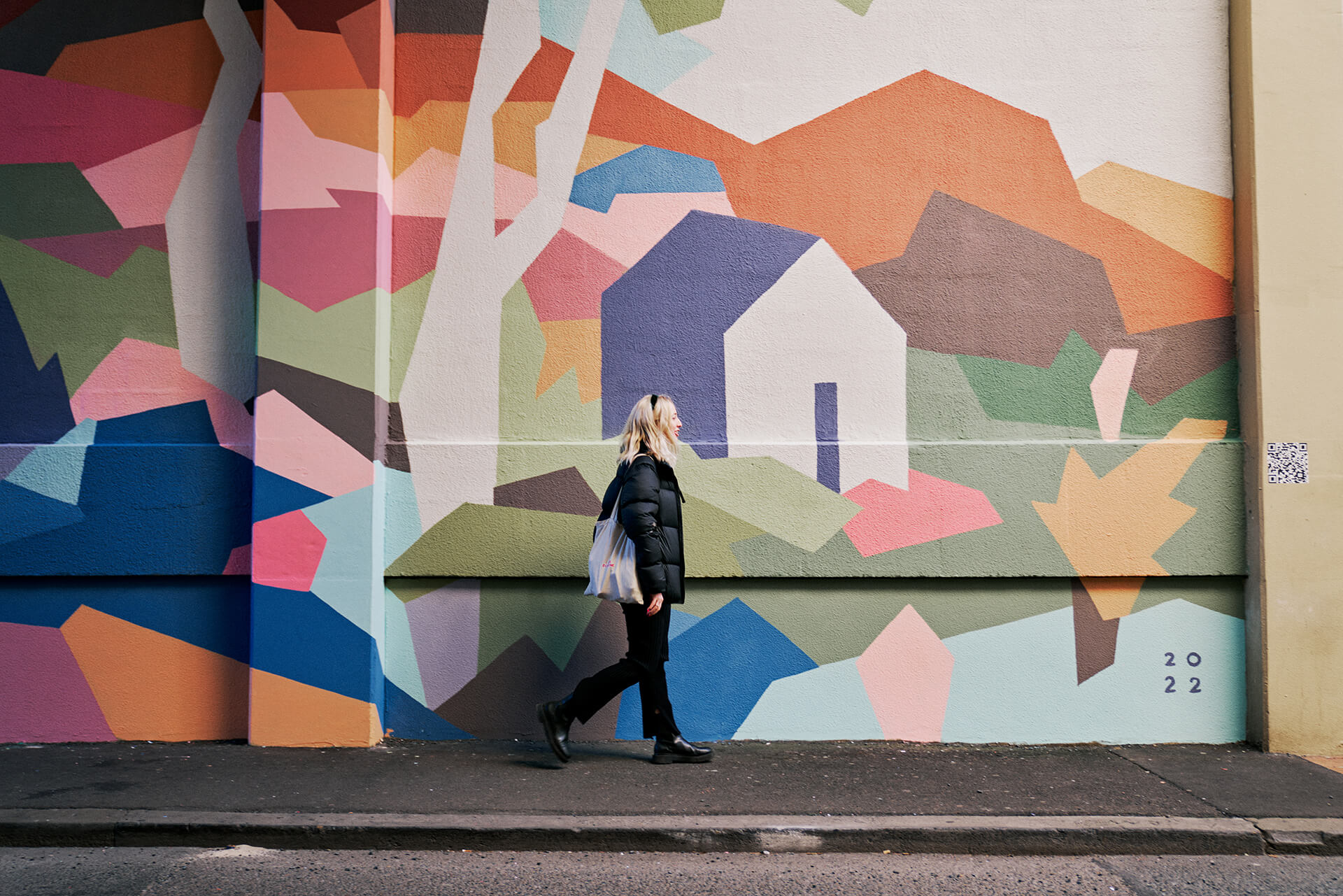 Woman walking past geometric multicoloured wall mural produced by VANDAL for Mirvac