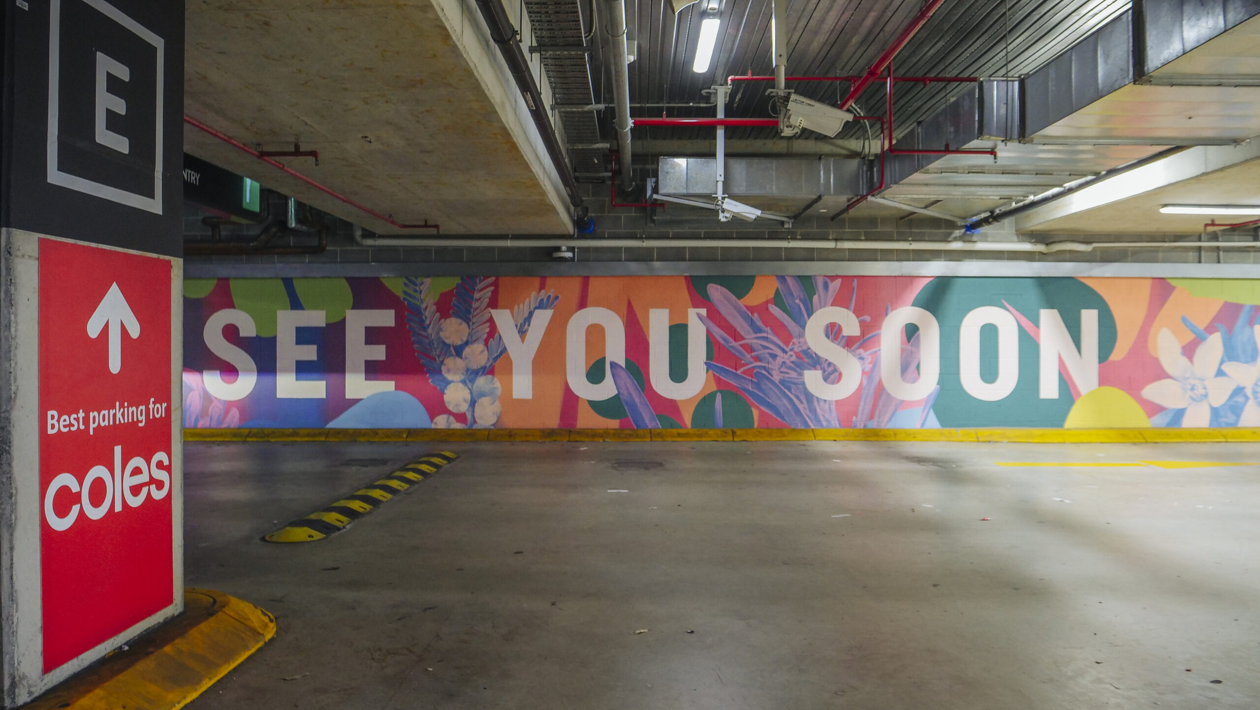 Geometric multicoloured wall mural featuring the phrase 'see you soon' placed in a shopping centre carpark exit produced by VANDAL for Mirvac